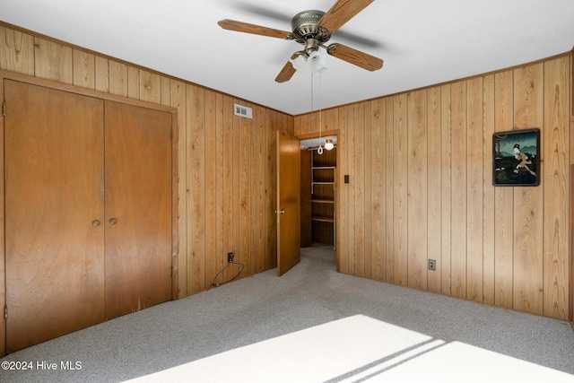 unfurnished bedroom featuring ceiling fan, wood walls, light carpet, and a closet