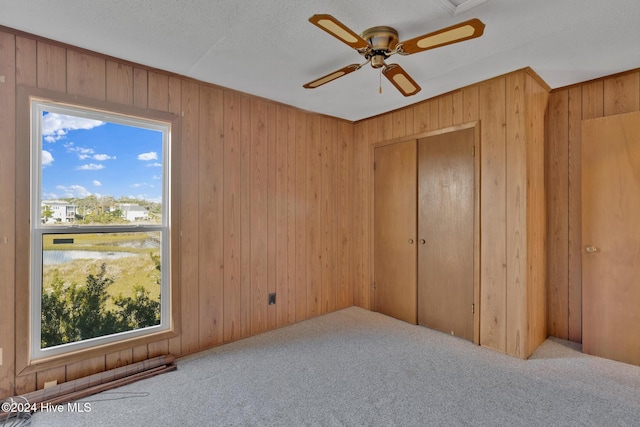 unfurnished bedroom featuring multiple windows, ceiling fan, wooden walls, and light carpet