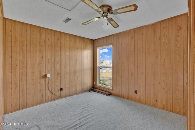 carpeted spare room featuring a textured ceiling, ceiling fan, and wooden walls