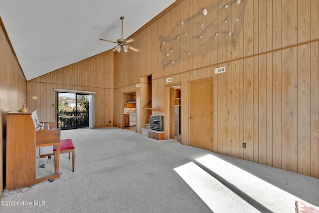 unfurnished living room featuring carpet flooring, high vaulted ceiling, ceiling fan, and wooden walls