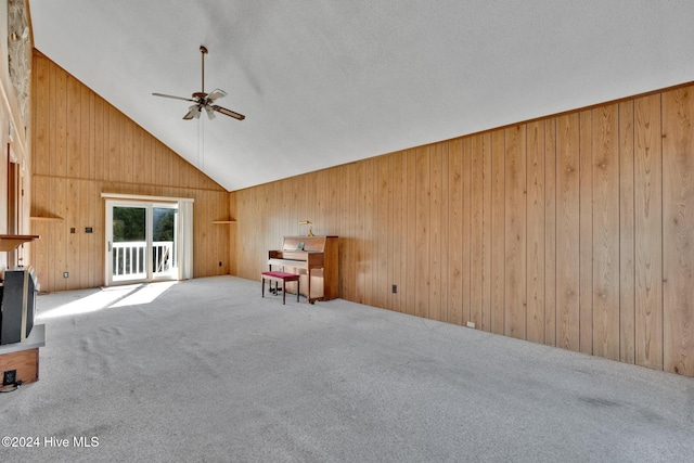 unfurnished living room featuring carpet, high vaulted ceiling, ceiling fan, and wooden walls