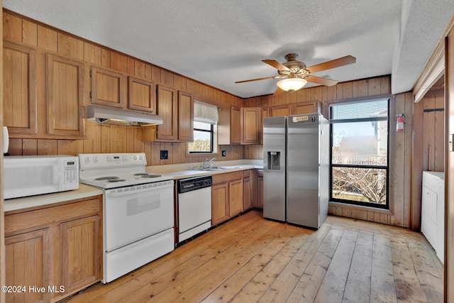 kitchen with a textured ceiling, white appliances, light hardwood / wood-style floors, and wood walls