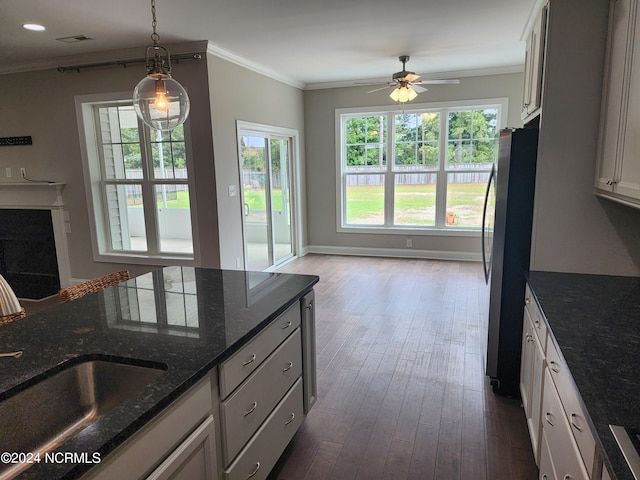 kitchen with white cabinetry, stainless steel refrigerator, decorative light fixtures, dark stone counters, and sink