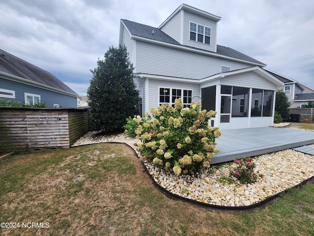 back of house featuring a deck, a sunroom, and a lawn