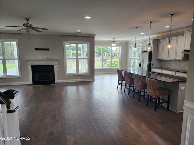 kitchen with hanging light fixtures, stainless steel fridge, white cabinetry, dark wood-type flooring, and a kitchen bar