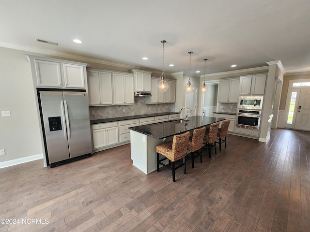 kitchen featuring pendant lighting, a center island with sink, a kitchen bar, appliances with stainless steel finishes, and hardwood / wood-style floors