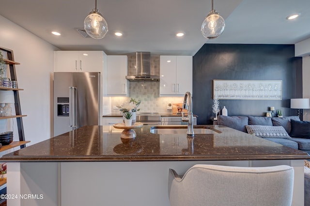 kitchen with pendant lighting, wall chimney range hood, sink, high quality fridge, and white cabinetry