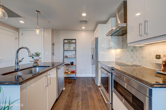 kitchen with sink, wall chimney range hood, pendant lighting, white cabinets, and an island with sink