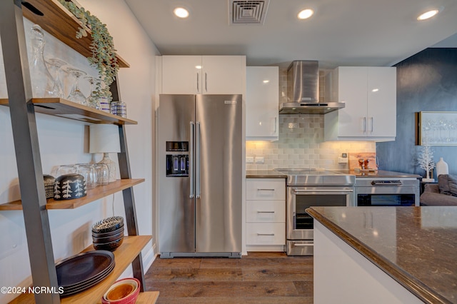 kitchen with wall chimney exhaust hood, stainless steel appliances, dark hardwood / wood-style flooring, dark stone counters, and white cabinets