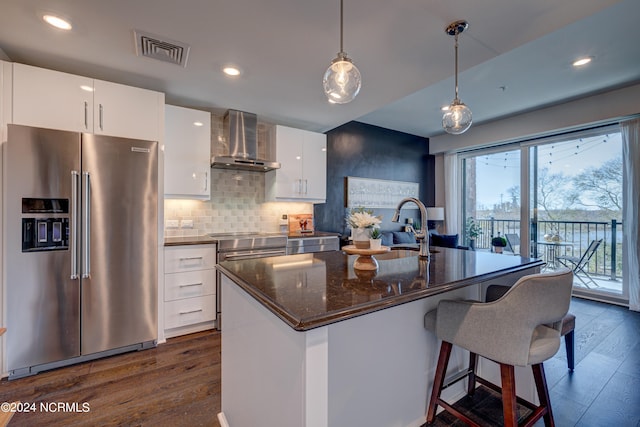 kitchen featuring white cabinetry, wall chimney exhaust hood, an island with sink, and appliances with stainless steel finishes