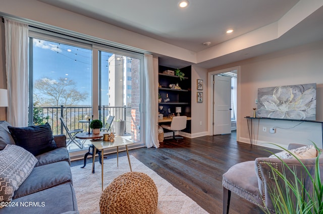 living room with a raised ceiling, built in features, dark wood-type flooring, and built in desk