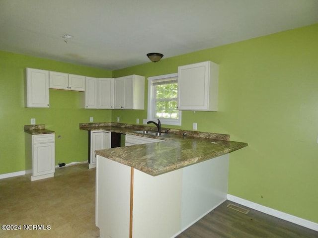 kitchen featuring visible vents, baseboards, a peninsula, white cabinets, and a sink