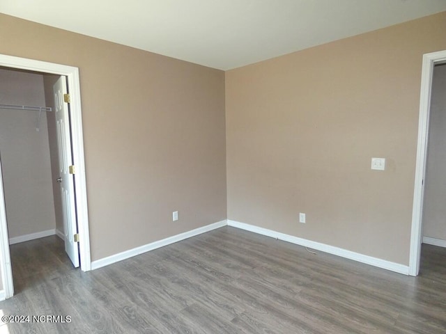 unfurnished bedroom featuring a closet, baseboards, a walk in closet, and dark wood-type flooring