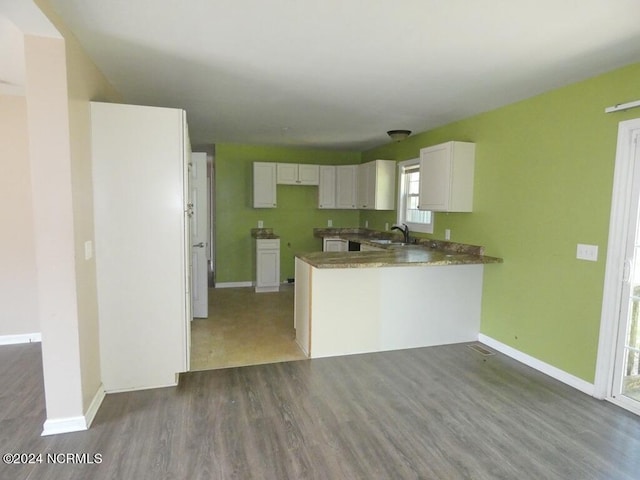 kitchen featuring wood finished floors, baseboards, a peninsula, a sink, and white cabinets