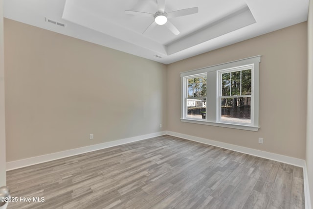 empty room featuring light wood-type flooring, ceiling fan, and a raised ceiling