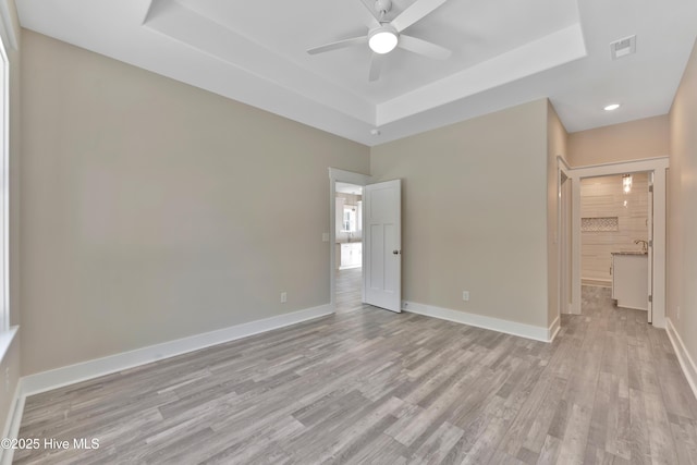 unfurnished bedroom with light wood-type flooring, ceiling fan, and a tray ceiling