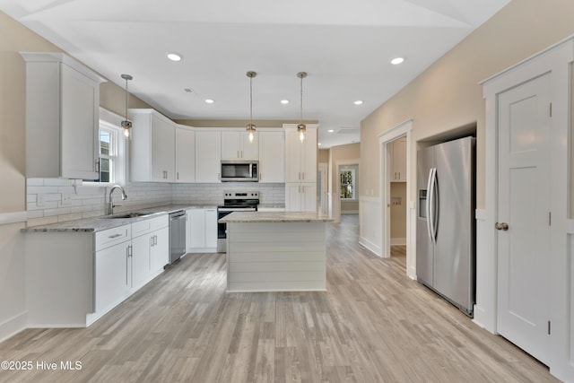 kitchen with a center island, hanging light fixtures, light stone countertops, stainless steel appliances, and white cabinets