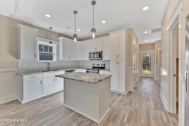 kitchen with appliances with stainless steel finishes, pendant lighting, white cabinets, and a center island