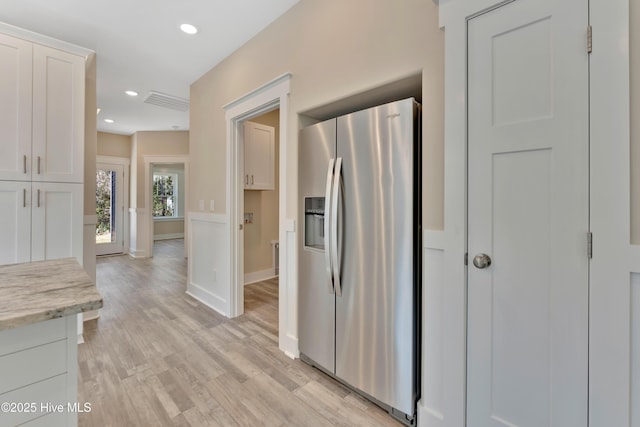 kitchen with white cabinets, stainless steel fridge with ice dispenser, light stone counters, and light hardwood / wood-style flooring