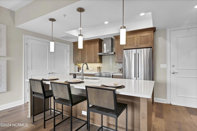 kitchen featuring decorative backsplash, light countertops, high quality fridge, a sink, and wall chimney range hood