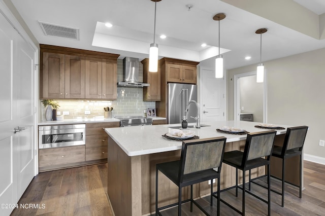 kitchen with wall chimney range hood, appliances with stainless steel finishes, dark wood-type flooring, and visible vents