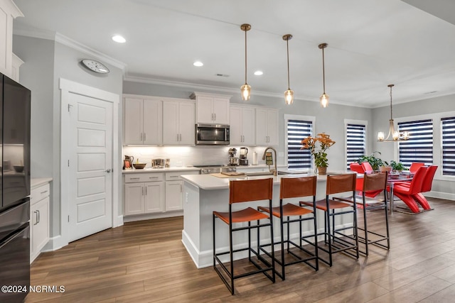 kitchen featuring a kitchen island with sink, fridge, dark hardwood / wood-style flooring, hanging light fixtures, and white cabinets