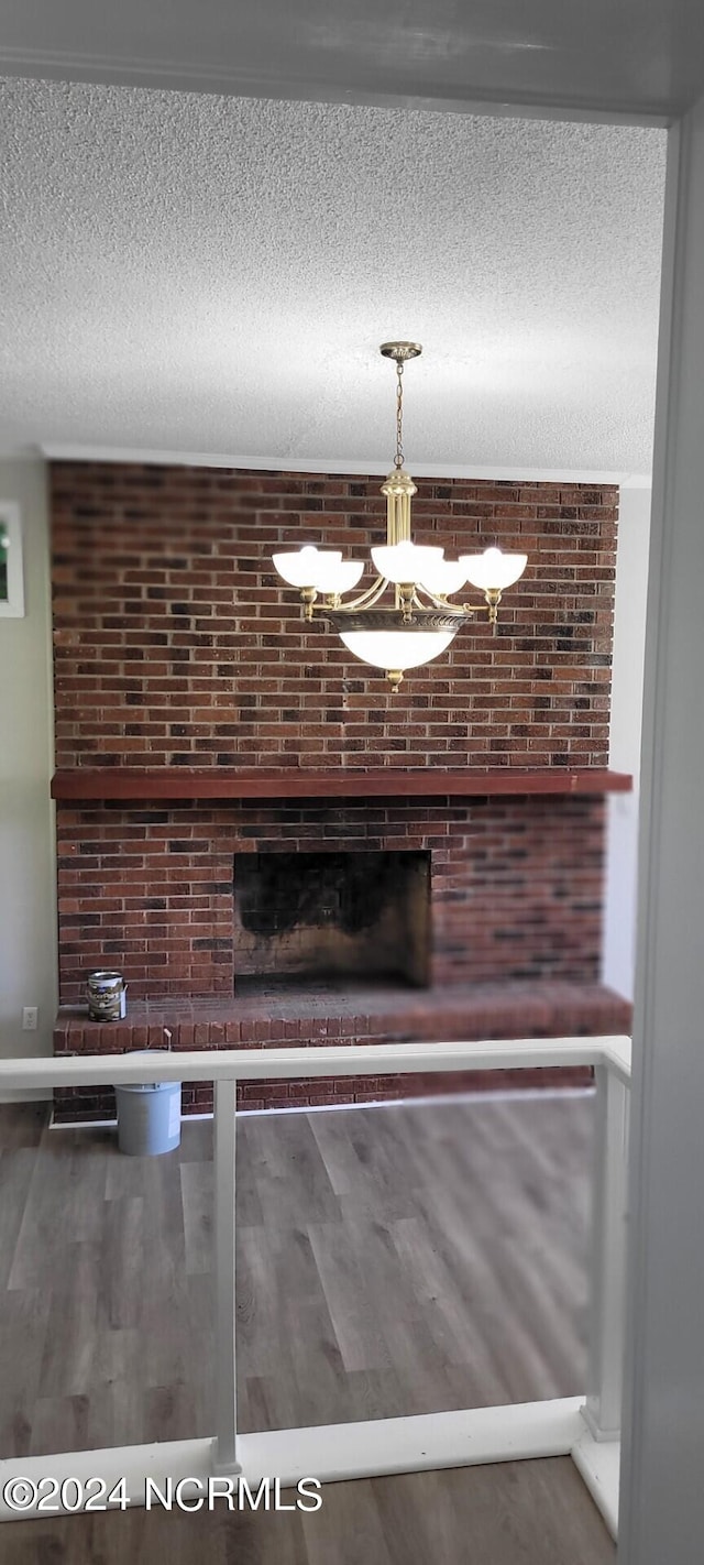 interior space featuring a brick fireplace, a chandelier, brick wall, wood-type flooring, and a textured ceiling