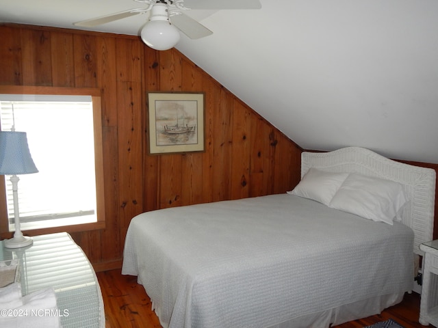 bedroom with lofted ceiling, ceiling fan, wooden walls, and dark hardwood / wood-style flooring