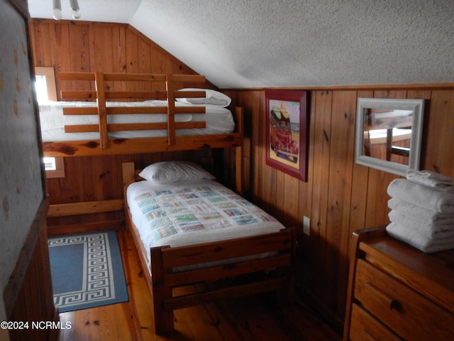 bedroom with lofted ceiling, hardwood / wood-style flooring, wooden walls, and a textured ceiling