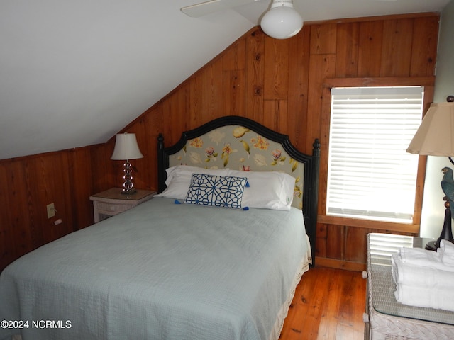 bedroom with vaulted ceiling, wood walls, ceiling fan, and hardwood / wood-style flooring