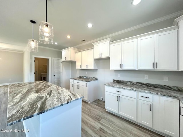 kitchen with a center island, white cabinets, hanging light fixtures, light wood-type flooring, and ornamental molding