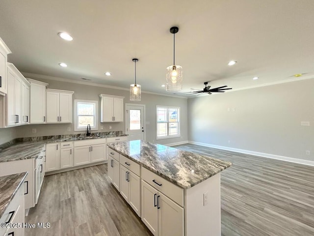 kitchen featuring a center island, sink, ceiling fan, light stone counters, and white cabinetry