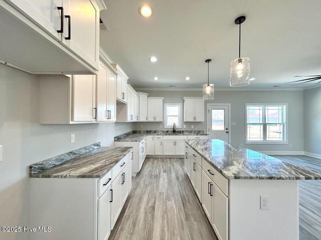 kitchen with a kitchen island, ceiling fan, sink, stone counters, and white cabinetry