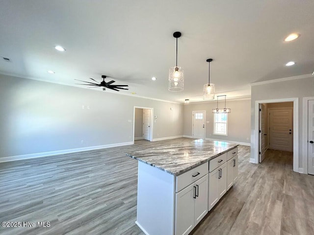 kitchen featuring ceiling fan, a center island, light stone counters, decorative light fixtures, and white cabinets