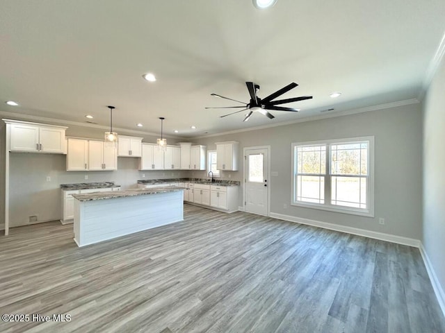 kitchen with decorative light fixtures, a kitchen island, white cabinetry, and crown molding