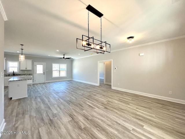 unfurnished living room with ceiling fan with notable chandelier, light hardwood / wood-style floors, and crown molding