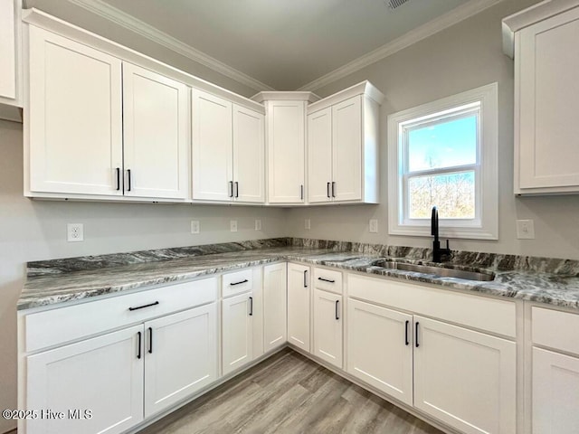 kitchen with white cabinetry, sink, crown molding, dark stone counters, and light wood-type flooring