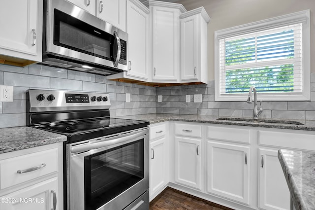 kitchen featuring white cabinets, backsplash, light stone countertops, stainless steel appliances, and sink