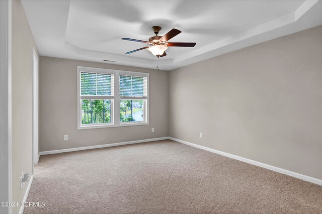 empty room featuring carpet flooring, a tray ceiling, and ceiling fan