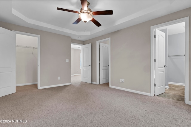 unfurnished bedroom with a raised ceiling, light colored carpet, a spacious closet, and ceiling fan