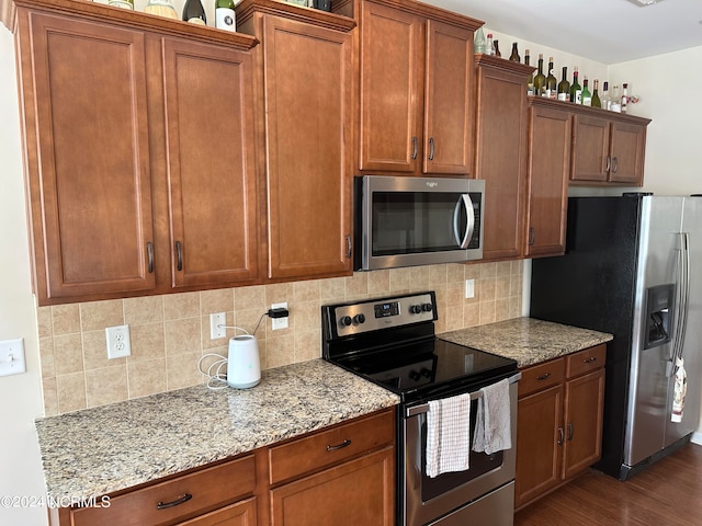 kitchen featuring backsplash, light stone counters, dark hardwood / wood-style flooring, and appliances with stainless steel finishes