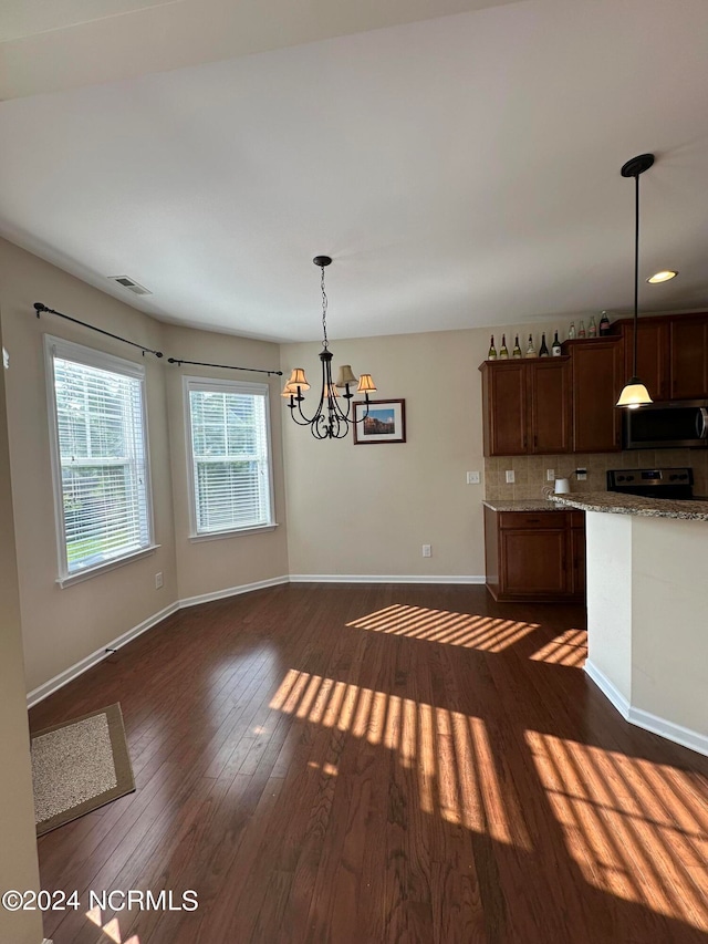 kitchen featuring pendant lighting, dark hardwood / wood-style floors, decorative backsplash, light stone counters, and a chandelier