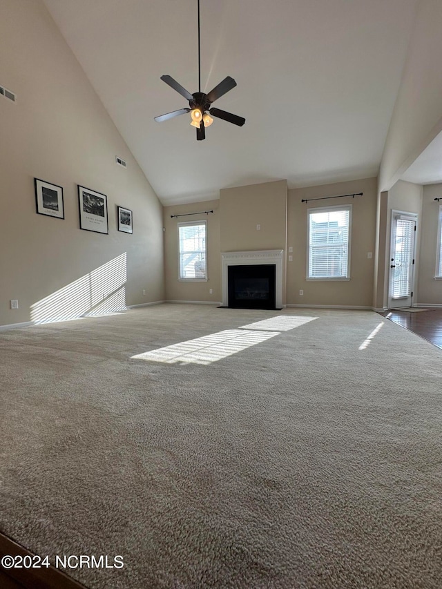 unfurnished living room with plenty of natural light, ceiling fan, carpet floors, and high vaulted ceiling