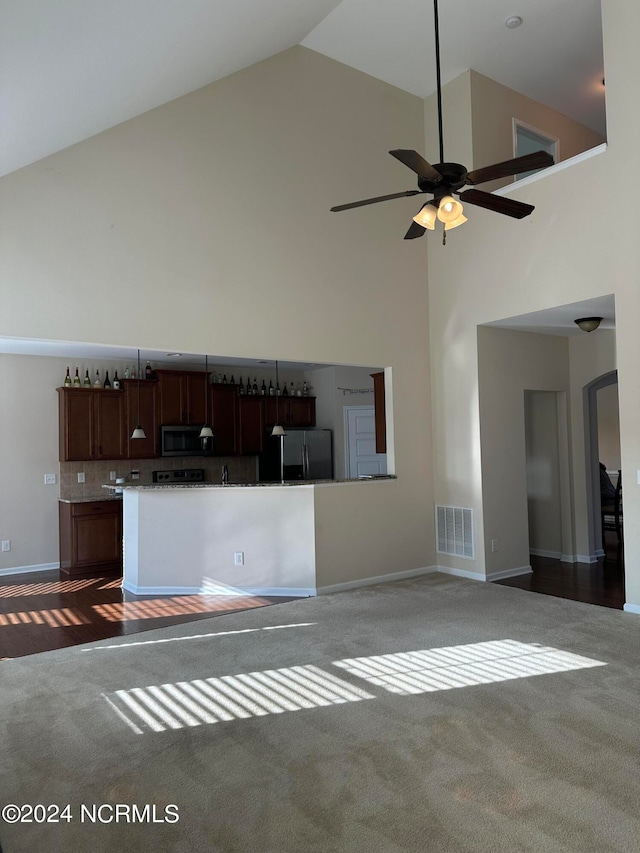 unfurnished living room with ceiling fan, high vaulted ceiling, and dark carpet