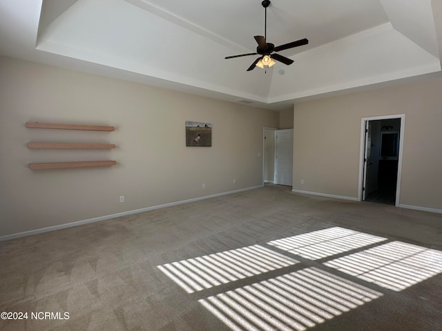 interior space featuring light carpet, connected bathroom, a raised ceiling, and ceiling fan