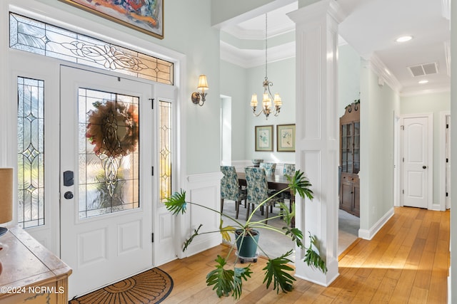 entryway with a raised ceiling, a notable chandelier, ornate columns, light hardwood / wood-style floors, and crown molding