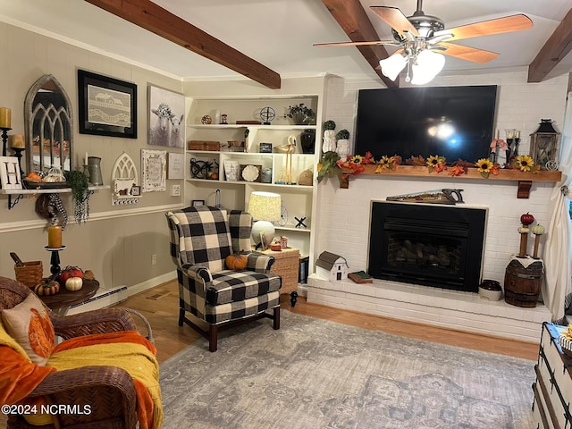 living room featuring ceiling fan, beamed ceiling, a brick fireplace, and wood-type flooring