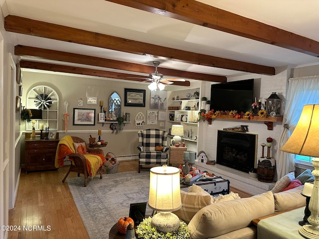 living room with beamed ceiling, hardwood / wood-style floors, ceiling fan, and a brick fireplace