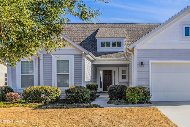 view of front of house featuring a garage, driveway, a front lawn, and roof with shingles