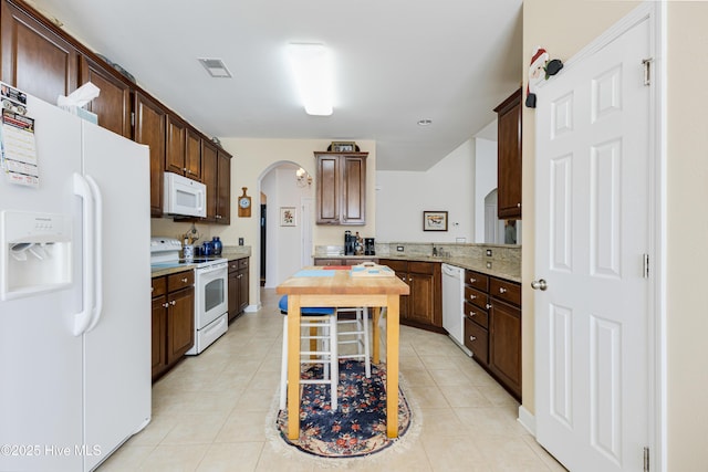 kitchen with arched walkways, light tile patterned flooring, dark brown cabinetry, white appliances, and visible vents